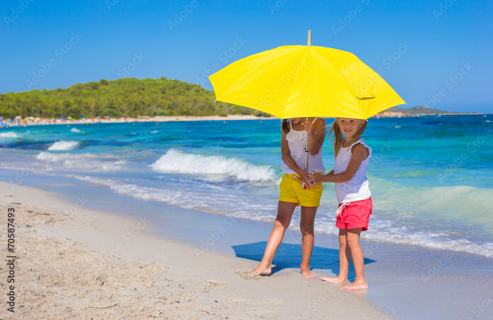 Little girls with big yellow umbrella walking on tropical beach Little girls with big yellow umbrella walking on tropical beach