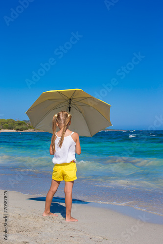Little cute girl with big yellow umbrella walking on tropical © travnikovstudio