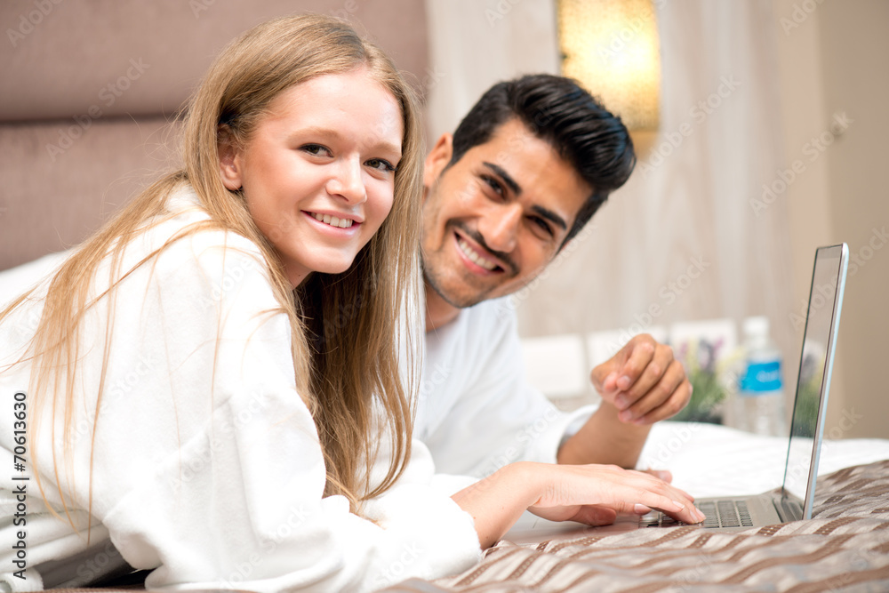 Smiling young couple using laptop in bed at home Smiling young couple using laptop in bed at home