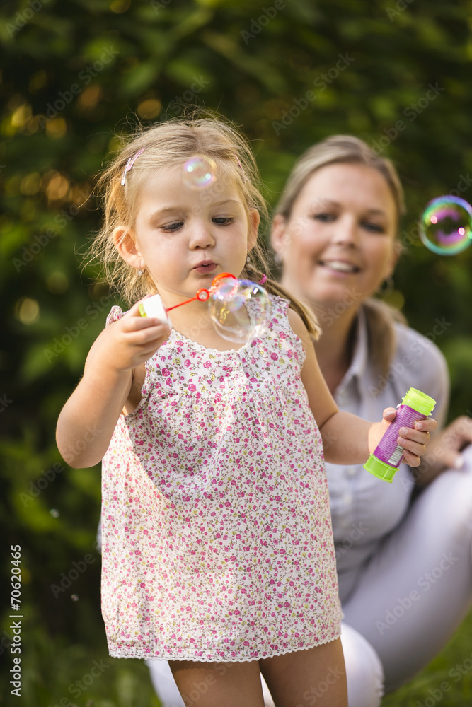 Mutter und Tochter blasen Seifenblasen im Garten Mutter und Tochter blasen Seifenblasen im Garten