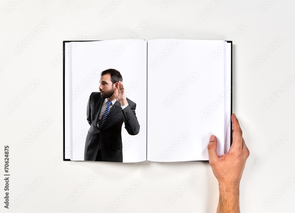 Young business man hearing something printed on book Young business man hearing something printed on book