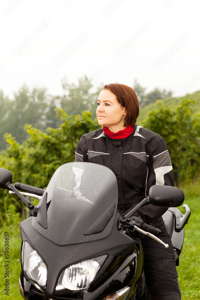 Motorradfahrerin sitzt mit Blick in die Ferne auf dem Motorrad