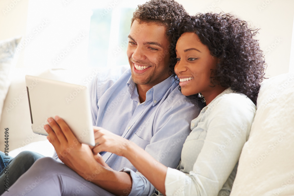 Young Couple Sitting On Sofa Using Digital Tablet Young Couple Sitting On Sofa Using Digital Tablet