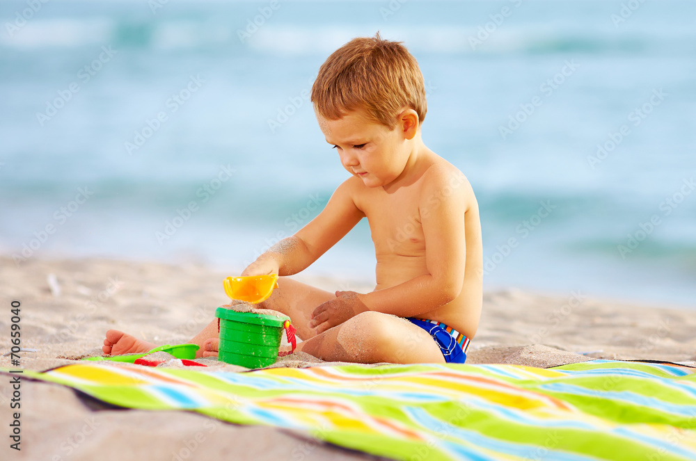 cute kid playing with toys in sand on the beach