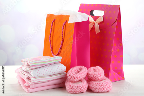 Baby clothes and gift bags on bright background