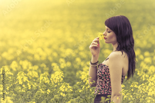 Beautiful woman in meadow of yellow flowers sniffing flower