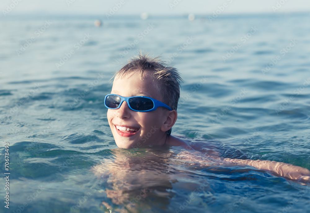 Funny little child with sunglasses swimming in sea 