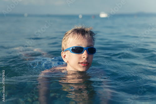 Funny child with sunglasses swimming in sea.
