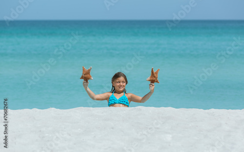 Little joyful smiling girl sitting at white sand tropical beach