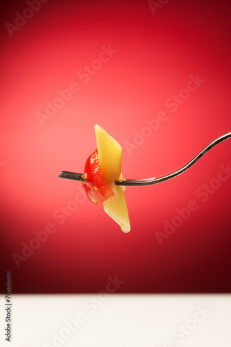 Fork with pasta and tomato on a red background