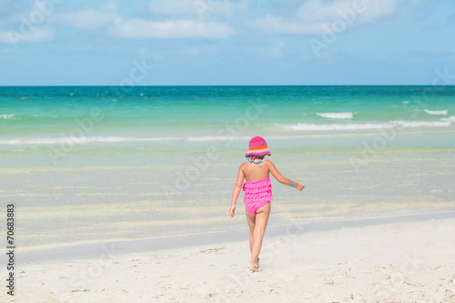 little girl in swimsuit walking on white sand beach near ocean