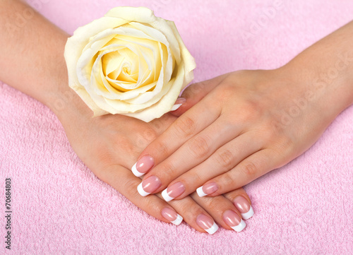 Female hands with french manicure decorated with rose on towel