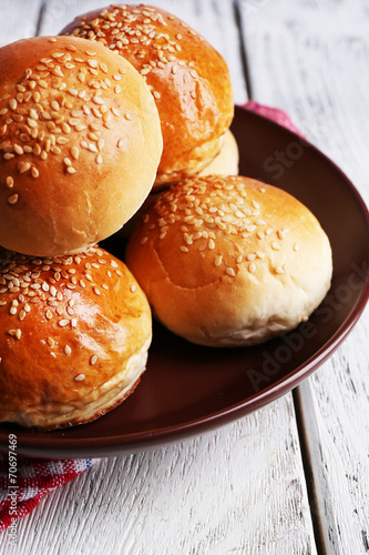 Tasty buns with sesame on plate, on color wooden background © Africa Studio