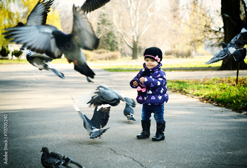 Cute fashionable baby girl feeding a pigeons at the autumn park