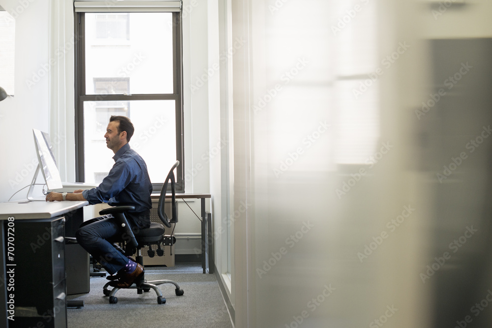 Office life. A man in casual clothing seated at a desk looking at a computer screen. Office life. A man in casual clothing seated at a desk looking at a computer screen.