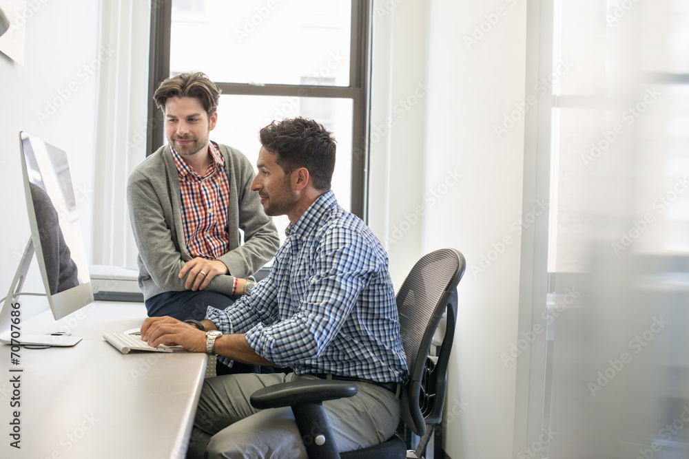 Two business colleagues in an office talking and referring to a computer screen. Two business colleagues in an office talking and referring to a computer screen.