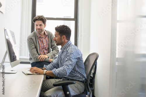 Two business colleagues in an office talking and referring to a computer screen. 