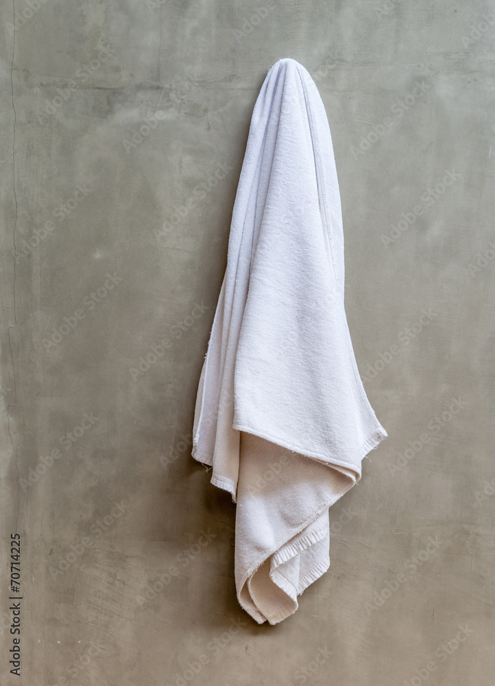 Fototapeta premium Hanging white towel draped on exposed concrete wall in the bathr