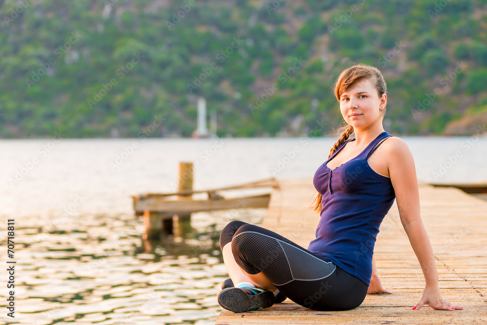 young brunette sitting on a pier in the lotus position