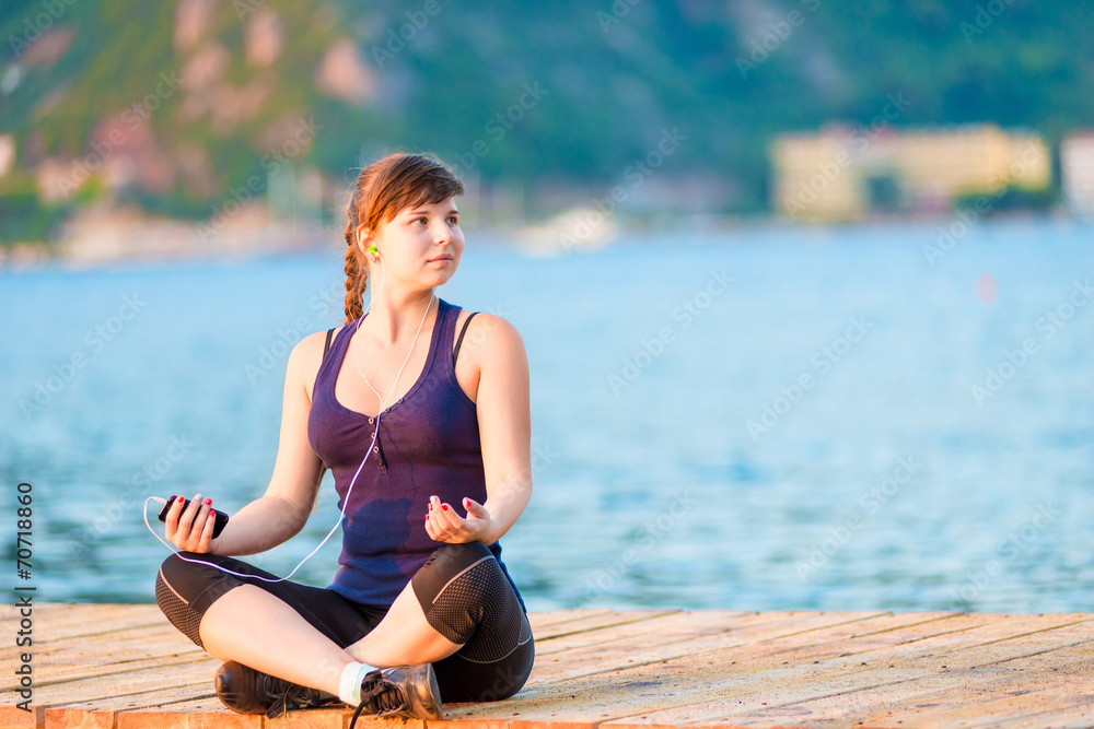 Young girl in lotus listening to music while sitting on a pier