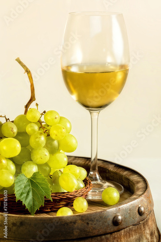 Glass of white wine and grapes on old barrel, in light cellar.