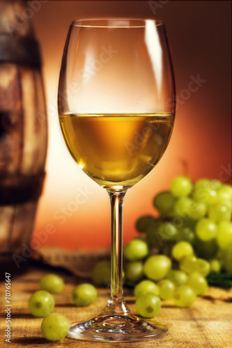 Glass of white wine in front of green grapes and old barrel