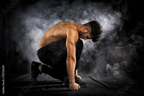 Obraz na plátně Handsome shirtless muscular young man kneeling down on black