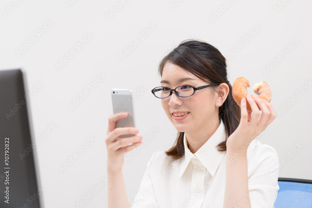 ドーナツを食べながらスマートフォンを見る女性