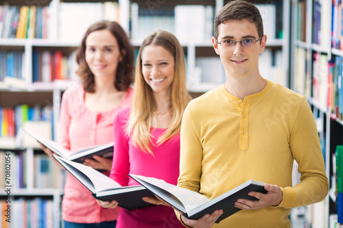 Group of three people holding books in library