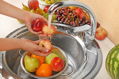 Fototapeta Naklejka Na Ścianę i Meble -  Woman's hands washing peaches and other fruits in colander in