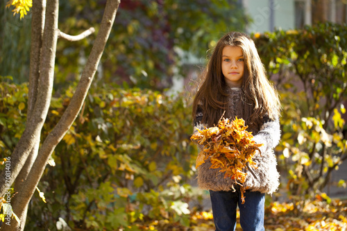 Young beautiful little girl with yellow leaves in autumn park