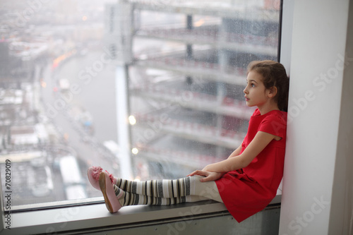 Little girl sitting on the windowsill of a large window