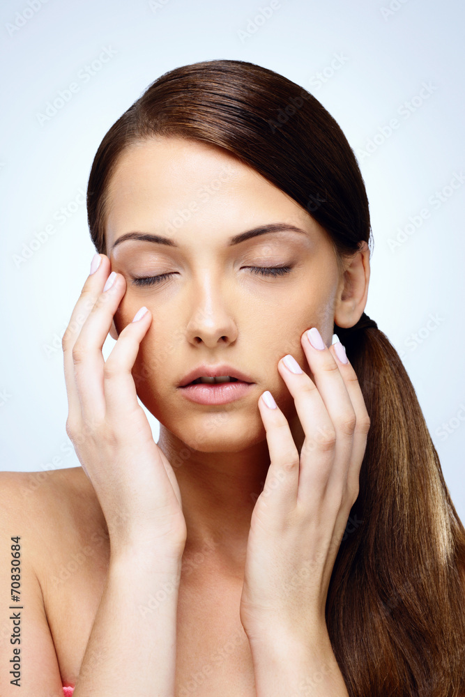 Beautiful young woman with eyes closed touching her face Beautiful young woman with eyes closed touching her face