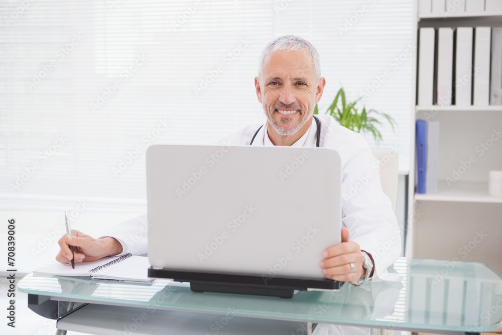 Smiling doctor using laptop and writing Smiling doctor using laptop and writing