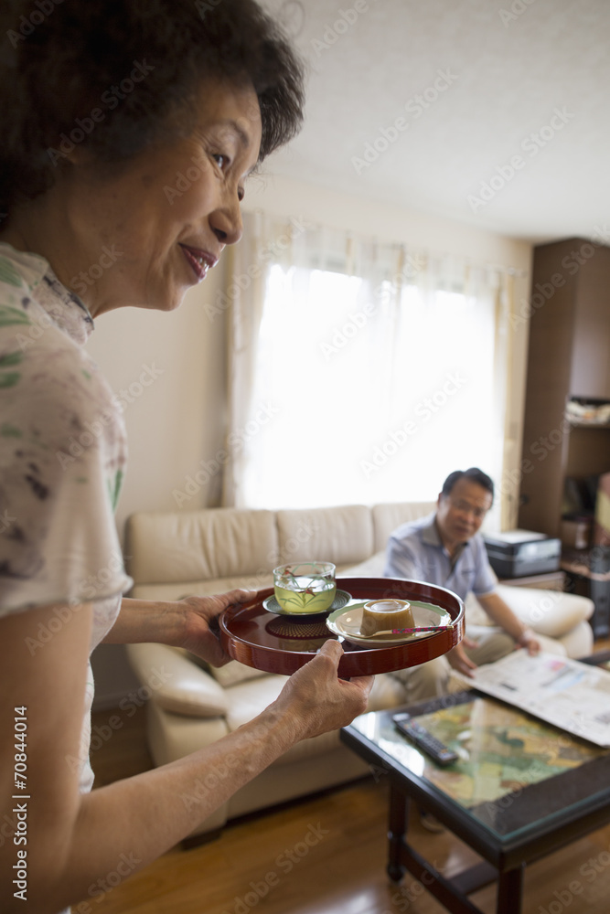 A woman serving a tray of food to a man sitting on a sofa.