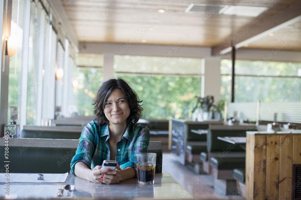 A woman in a checked shirt sitting at a table, laughing and looking at her smart phone. A woman in a checked shirt sitting at a table, laughing and looking at her smart phone.
