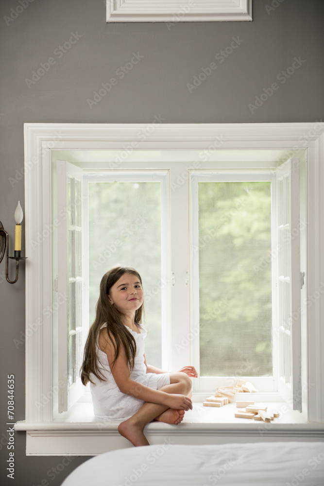 A girl in a white dress seated by a window playing. A girl in a white dress seated by a window playing.