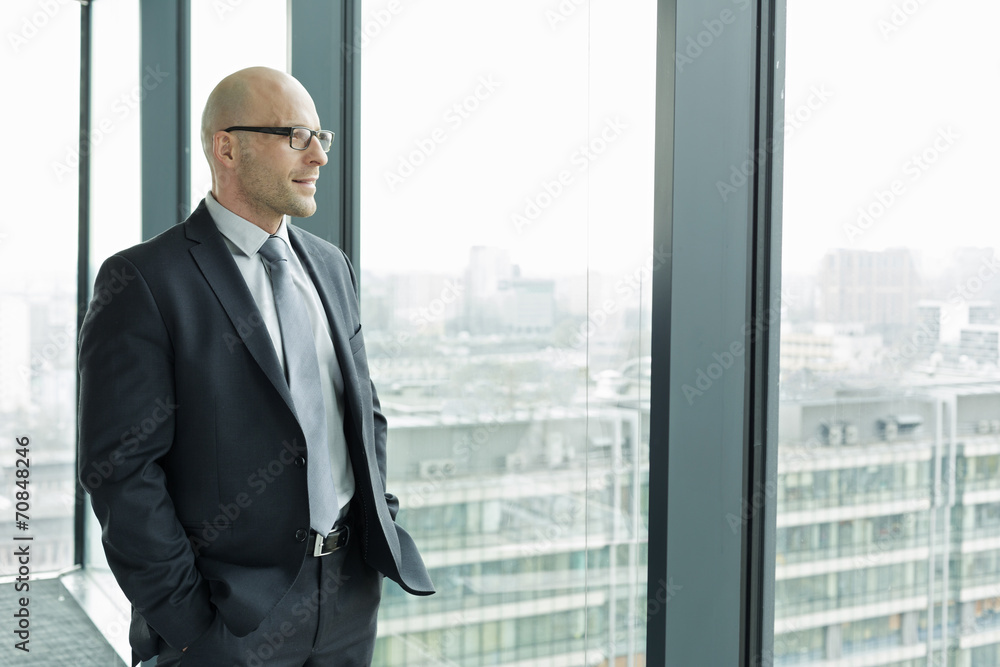 Confident businessman on office floor looking out of window Confident businessman on office floor looking out of window