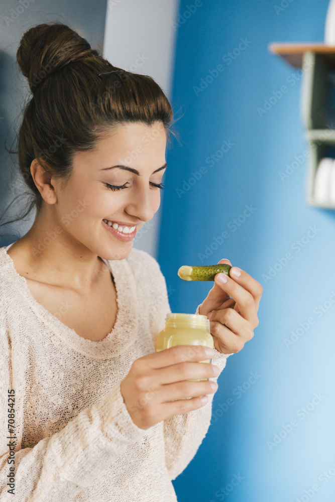 Portrait of young pregnant woman eating pickled gherkin with mustard in her kitchen Portrait of young pregnant woman eating pickled gherkin with mustard in her kitchen