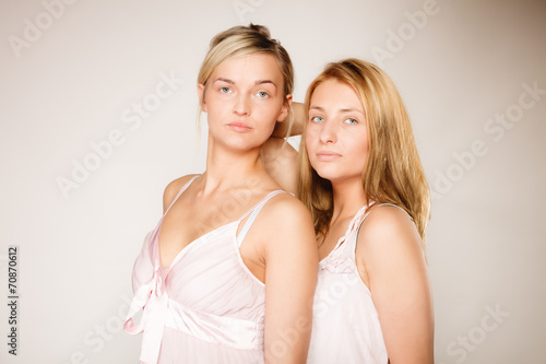 Two blonde women with no makeup on gray