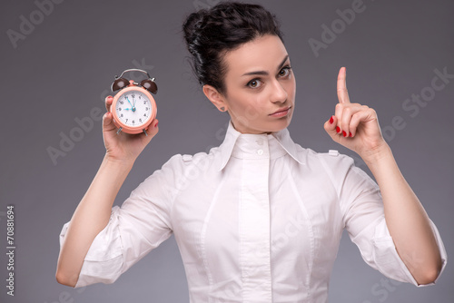 Portrait of pretty girl holding an alarm clock in her hand showi