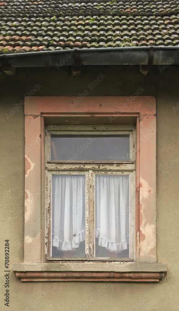 Marodes renovierungsbedürftiges Fenster mit Gardinen