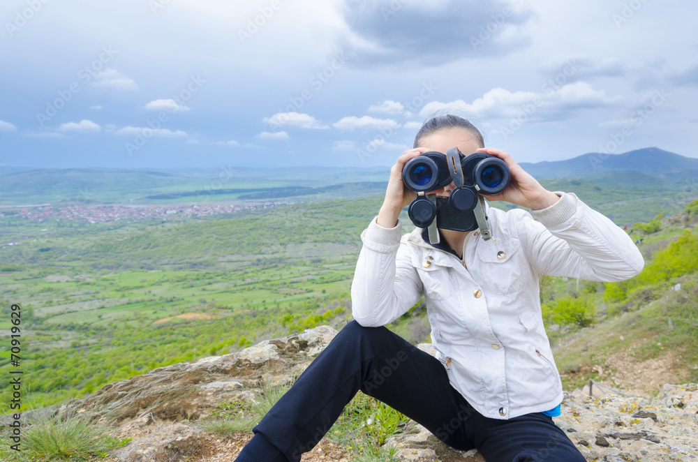 Girl sitting on rock and looking with binocular
