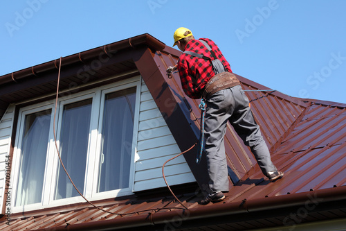 roofer builder worker spraying paint on metal sheet roof
