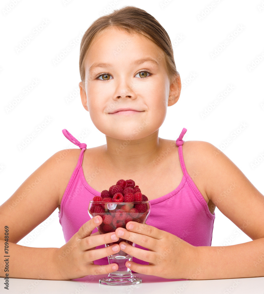 Happy little girl is eating raspberries