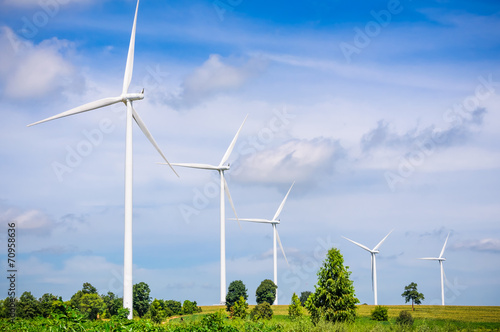 Wind turbine on the green meadow over the blue clouded sky