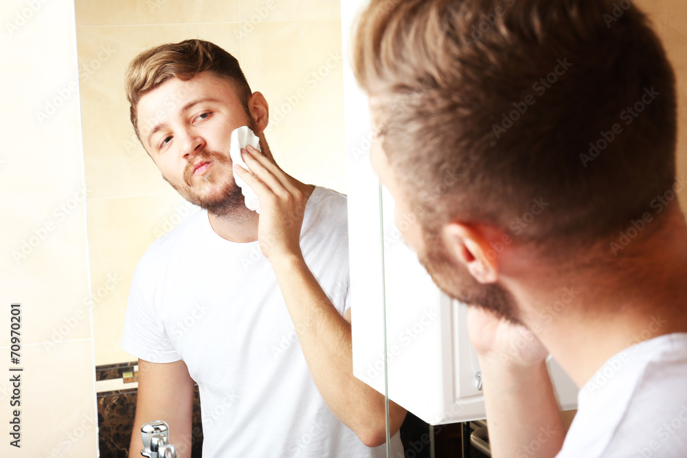 Young man shaving his beard in bathroom Young man shaving his beard in bathroom
