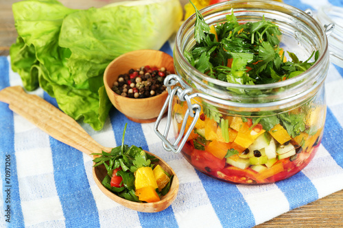 Vegetable salad in glass jar, on napkin, on wooden background