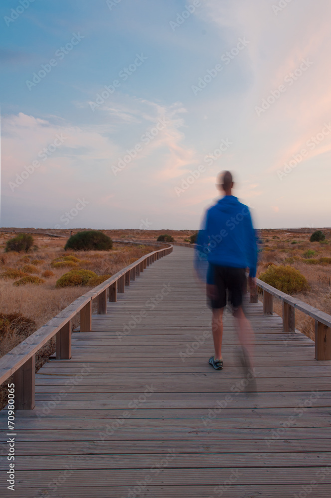 Man walking by a wooden footbridge. Dunes, Algarve, Portugal