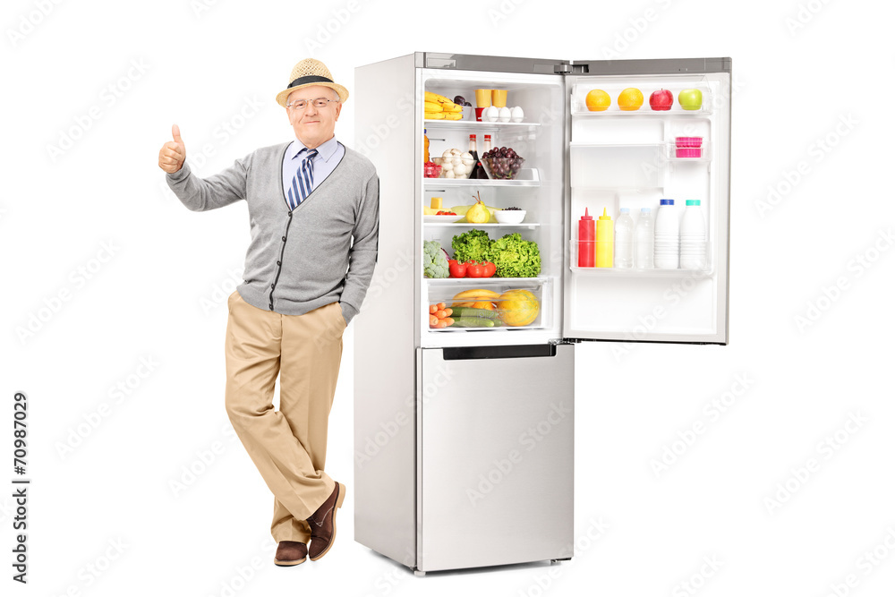 Fototapeta premium Senior leaning on a fridge and giving thumb up